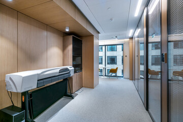 Modern workspace with large printer and glass meeting rooms in a sleek office building.