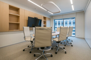 A contemporary conference room features a circular table surrounded by ergonomic chairs and a large display screen, illuminated by natural light from wide windows...