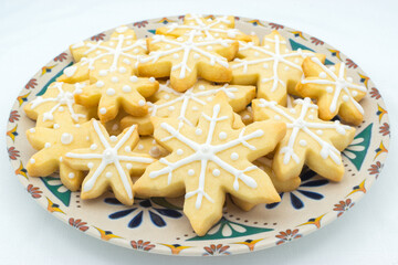Plate with snowflake-shaped sugar icing Christmas cookies. Disposed on a white tablecloth as background.