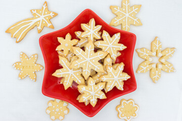 Red star-shaped plate with Christmas sugar icing cookies. Some spare cookies around. Top view on a white tablecloth as background.