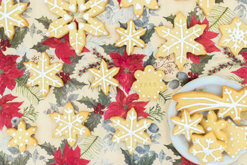 Snowflake-shaped sugar icing Christmas cookies, on a tablecloth with a Christmas pattern. Top view.
