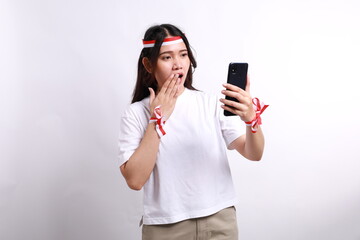 Surprised young Asian woman wearing red white flag ribbon read a promotion online on smartphone...