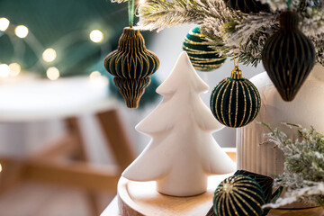A bouquet of fir trees, a plaid, a white ceramic Christmas tree and paper toys on a wooden table in the home interior of the living room. A cozy concept for a festive home decoration.