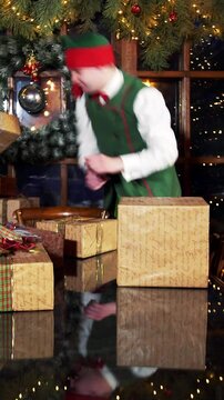Happy boy working with Christmas presents. Elves put gift boxes on the table in the Christmas decorated room in Santa's residence. Vertical video.
