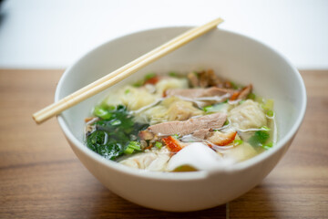 Pork dumplings Wonton Soup with bok choy and Barbecued red pork serve with chopsticks on a bowl on wooden table and sunlight background