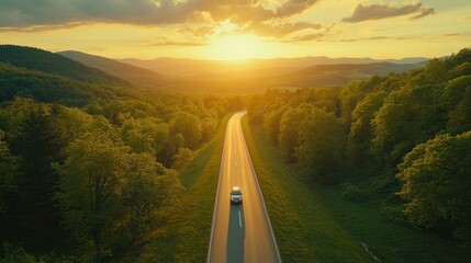 Aerial view natural landscape of car driving on a highway road in a green forest with trees, meadow and sunset.