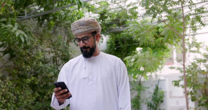Omani man wearing omani traditional dishdasha and Musaar is looking at his cell phone