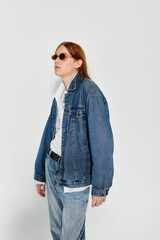 A teenage boy with long red hair exudes confidence in a denim ensemble set against a minimalist...