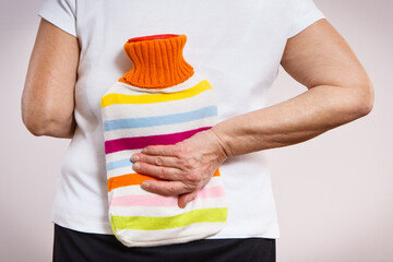 Senior woman with hot water bottle on her back. Help with pain in old age