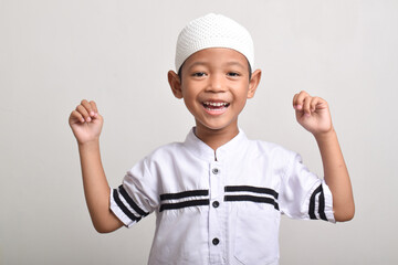 A happy and excited Muslim Asian boy with raised hands isolated on white background