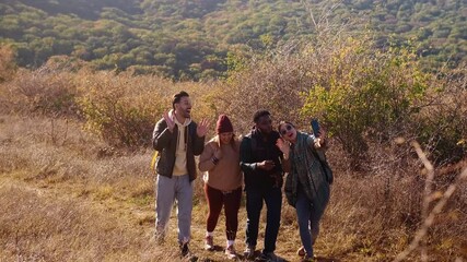 Smiling group of friends having fun while hiking together on hill at sunset and making video blog with smart phone.