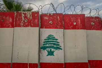Fototapeta premium The Lebanon flag image on the concrete fence with barbed wire, at conflict region of Middle East, in Lebanese city of Beirut. 