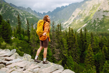 Naklejka premium Happy woman tourist with backpack enjoys the beautiful scenery of the majestic mountains. Adventure, travel concept.