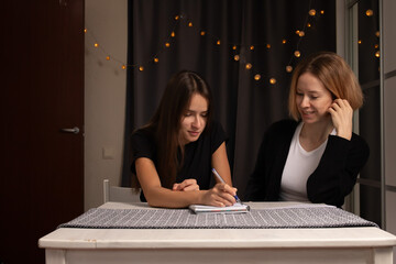 Mother and Daughter Writing in Notebook Together, writing and study session, mother guiding daughter in learning
