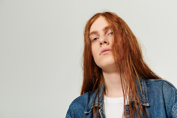 A confident teenager with flowing red hair displays his trendy denim ensemble against a simple backdrop.