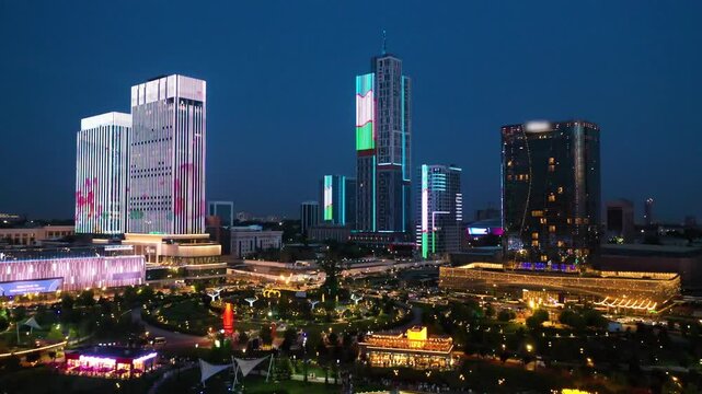 Tashkent City illuminated at night, surrounded by modern skyscrapers with bright LED displays and a lake reflecting city lights