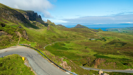 A winding road descends into the breathtaking Quiraing on the Isle of Skye, Scotland, showcasing lush green landscapes, dramatic cliffs, and stunning coastal views.