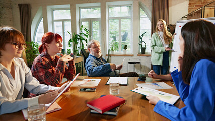 Obraz premium Group of business professionals carefully reviewing reports and data around conference table in modern office. Corporate discussions. Concept of business, consultation, marketing, management. Ad