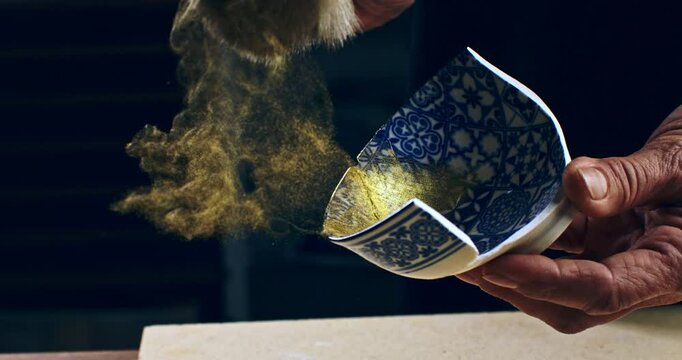 Super slow motion close up of painting brush is being moved with flying gold shimmer powder dust particles splash explosion isolated on soft dark background at 1000 fps.