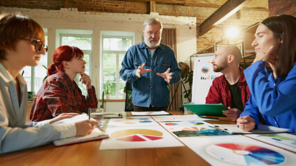 Professional team gathers around conference table, analyzing business data and discussing company growth strategies in modern office setting. Concept of business, consultation, marketing, management.