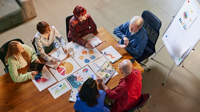 Aerial view of corporate meeting focused on data analysis and planning, with team members reviewing reports and discussing. Concept of business, consultation, marketing, management. Ad