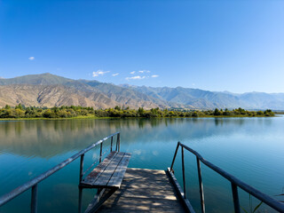 Fototapeta premium A wooden pier on Issyk-Kul lake with a view of the mountains. A beautiful spot for relaxation and enjoying the natural landscapes of Kyrgyzstan