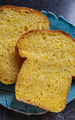 Two slices of beautiful appetizing handmade pumpkin bread on a blue plate located on a dark surface.