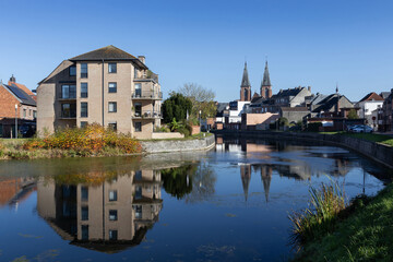 Obraz premium View of the Old Dender River, as it flows through Dendermonde in East Flanders Belgium on a sunny autumn day. The twin spires of the Benedictine Abbey are reflected in the the calm water.