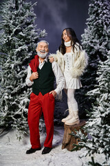 A joyful man and woman stand amidst snow covered trees, celebrating the festive season together.