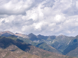 A picturesque view of majestic mountains with varying shades of green and brown, under a sky filled...
