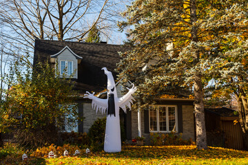 Pretty suburb house with tall ghost Halloween and smaller spooky decorations seen during a sunny...