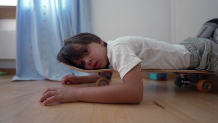 Young boy lying on a skateboard indoors, appearing deep in thought. a calm and introspective moment...