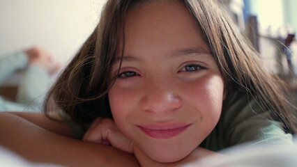 Young girl lying down, smiling gently with a calm and serene expression. The close-up shot captures...
