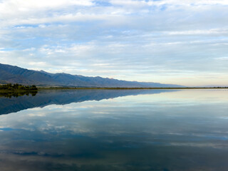 The calm waters of Issyk-Kul lake reflect dramatic clouds and mountains. Silence and tranquility in a natural oasis in Kyrgyzstan