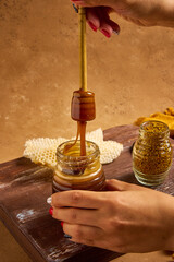 Still life of honey in a jar, honeycomb, pennyroyal and hands holding honey spoon dripping honey 