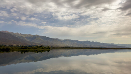 Obraz premium A quiet mountain lake Issyk-Kul, surrounded by green valleys and majestic mountains. The perfect spot for tourism and peaceful relaxation in Kyrgyzstan.