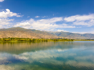 Obraz premium A quiet mountain lake Issyk-Kul, surrounded by green valleys and majestic mountains. The perfect spot for tourism and peaceful relaxation in Kyrgyzstan.