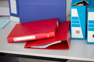 Deux classeurs rouges posés sur un bureau avec des boites d'archivage de documents bleues.