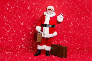 Full length body size view of nice attractive cheerful cheery fat bearded man carrying vintage heavy bag luggage baggage showing v-sign isolated on bright vivid shine red background