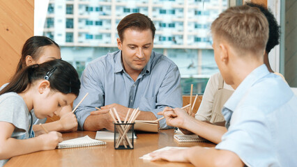 Smart highschool boy in casual shirt asking professional teacher while student with mixed races writing book. Caucasian instructor giving comment while creative child pointing at note. Edification.