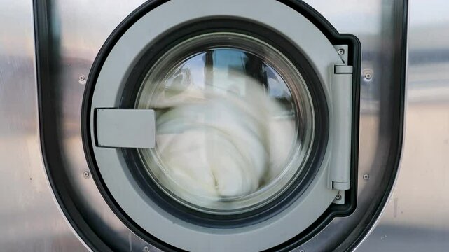 Machines &agrave; laver &ndash; Gros plan sur porte d'une machine &agrave; laver industrielle dans une laverie automatique publique avec une couette qui tourne dedans.