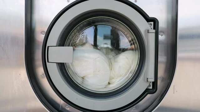 Machines &agrave; laver &ndash; Gros plan sur porte d'une machine &agrave; laver industrielle dans une laverie automatique publique avec une couette qui tourne dedans.