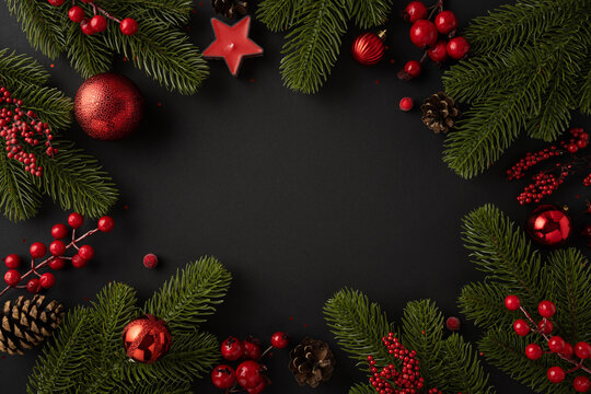 Top view of Christmas decorations including pine branches, red ornaments, and berries. A festive holiday arrangement with a black background, conveying warmth and celebration