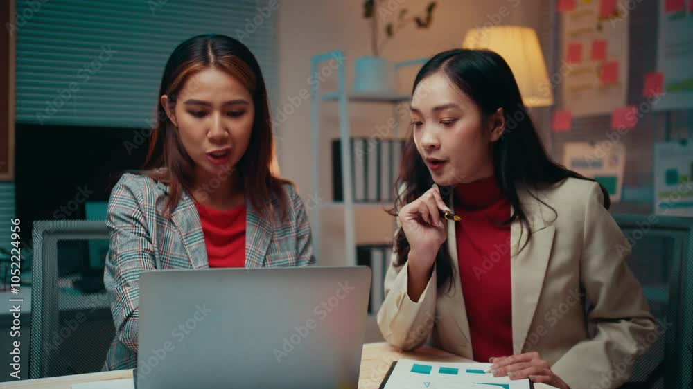 Poster two businesswomen are working late in their office. they are discussing a project and looking at a l