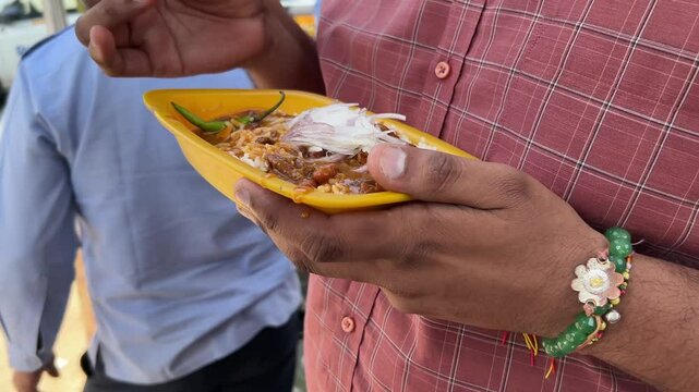 man's hands holding a plate of Usal Sev and a plastic spoon, eating in the street in India