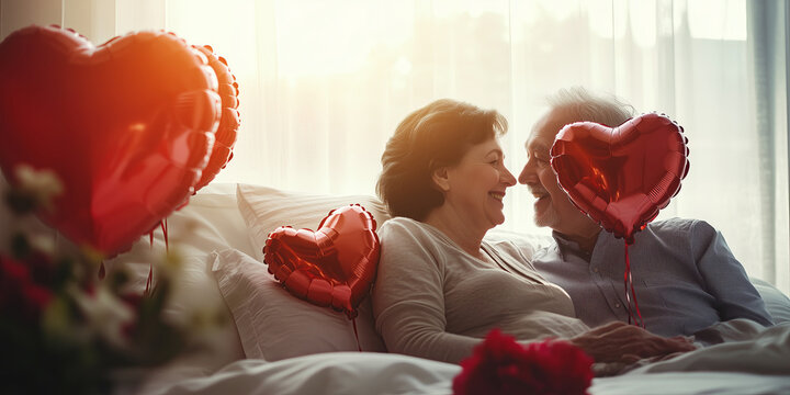 Senior couple lying in bed with red heart shaped balloons and flowers on a Valentine day. - Powered by Adobe