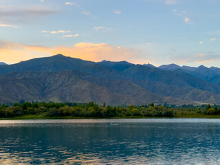 Obraz premium Quiet mountain lake, evening light on the water, Kyrgyzstan. Still water and mountain reflection in the lake