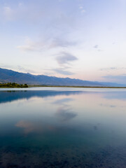 Fototapeta premium Quiet mountain lake, evening light on the water, Kyrgyzstan. Still water and mountain reflection in the lake