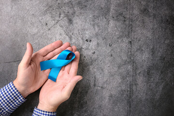 Top view of male hands holding blue ribbon international symbol on dark abstract background.