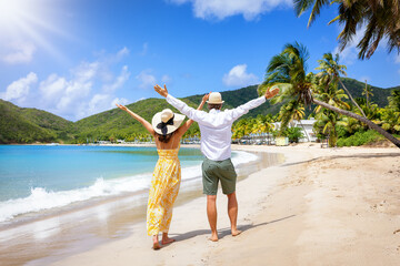 Happy holiday couple with sunhats enjoys a tropical beach with palm trees in the Caribbean Islands